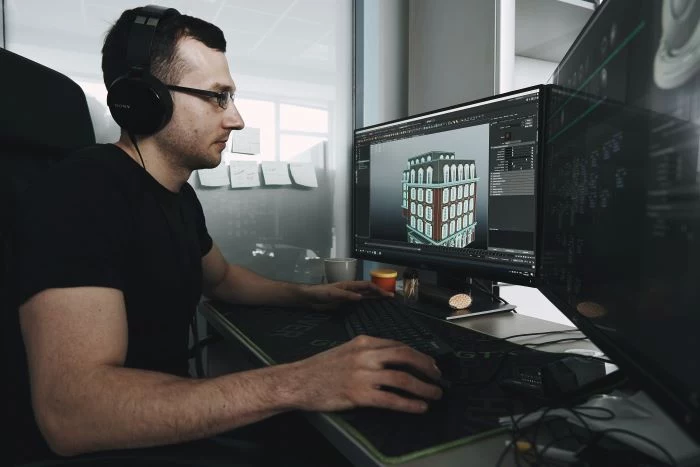 man sitting in front of computer monitors reality capture 3d rendered image of building