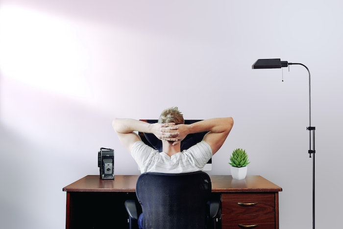 man sitting on black office chair in front of desk working from home mac desktop computer on it potted succulent