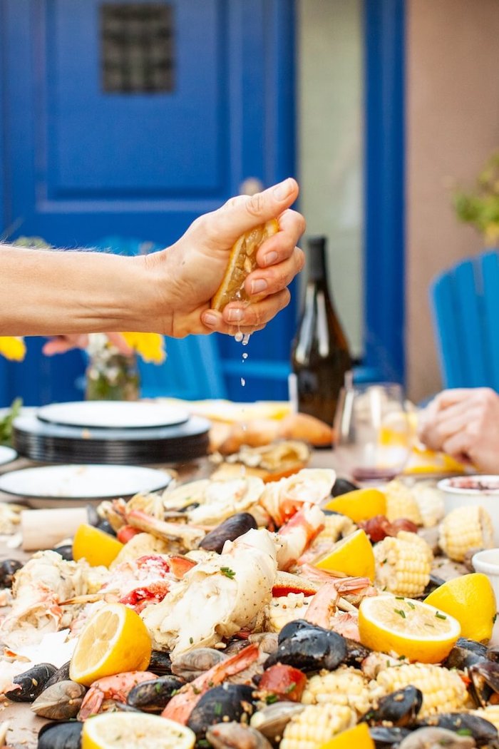 man sqeezing lemon over table with seafood boil in the middle shrimp boil recipe with potatoes corn on the cob