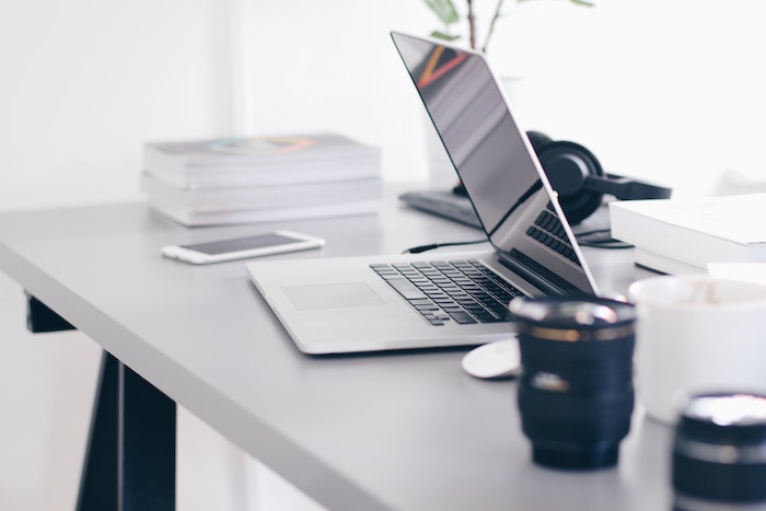 office desk with open laptop phone next to it working from home books headphones coffee mug on the desk