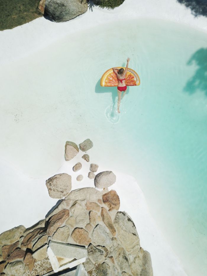 orange slice float woman leaning on it in clear turquoise water beach background images rocks around the water