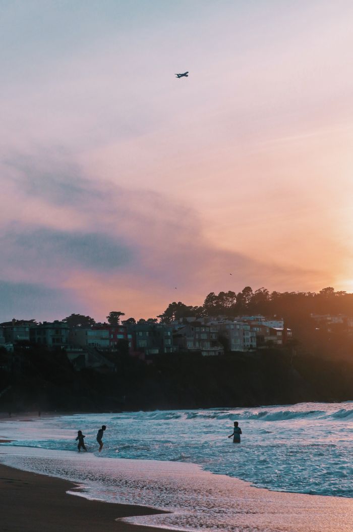 plane in the sky above the sea summer aesthetic wallpaper waves crashing into the beach three people in the water