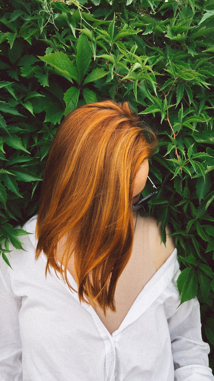 red hair best hair mask woman with medium length straight hair wearing white shirt green bush behind her