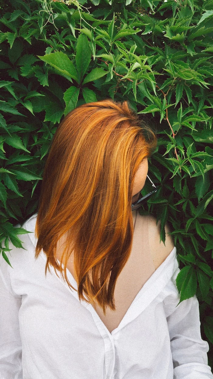 red hair best hair mask woman with medium length straight hair wearing white shirt green bush behind her