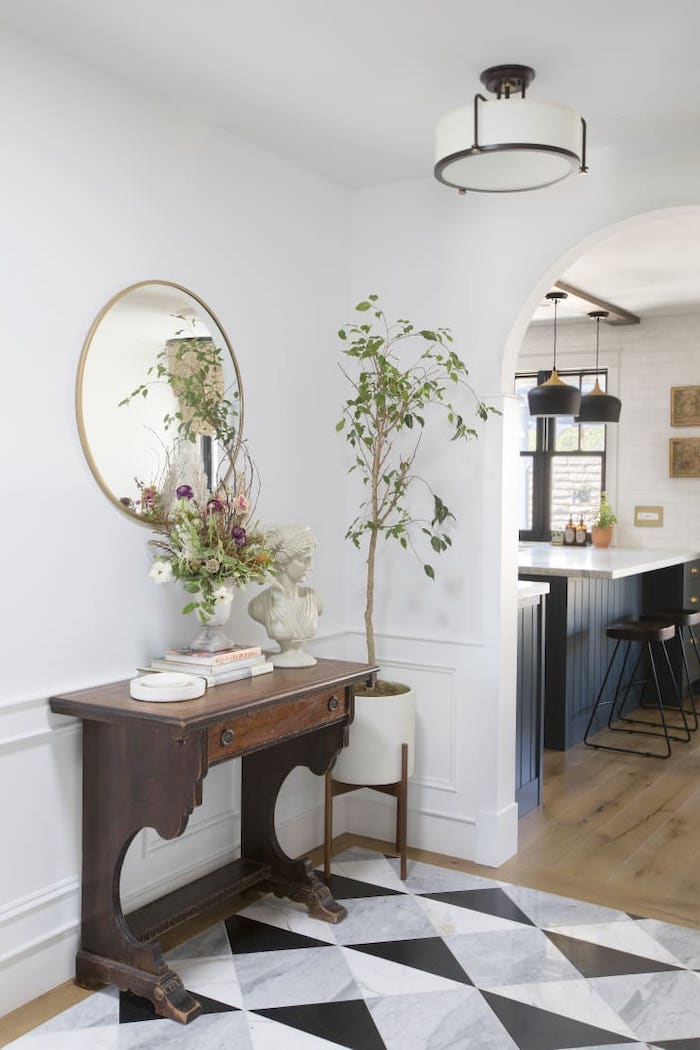 round mirror hanging on white wall above vintage cupboard hallway wall decor ideas gray black and white tiles on the floor