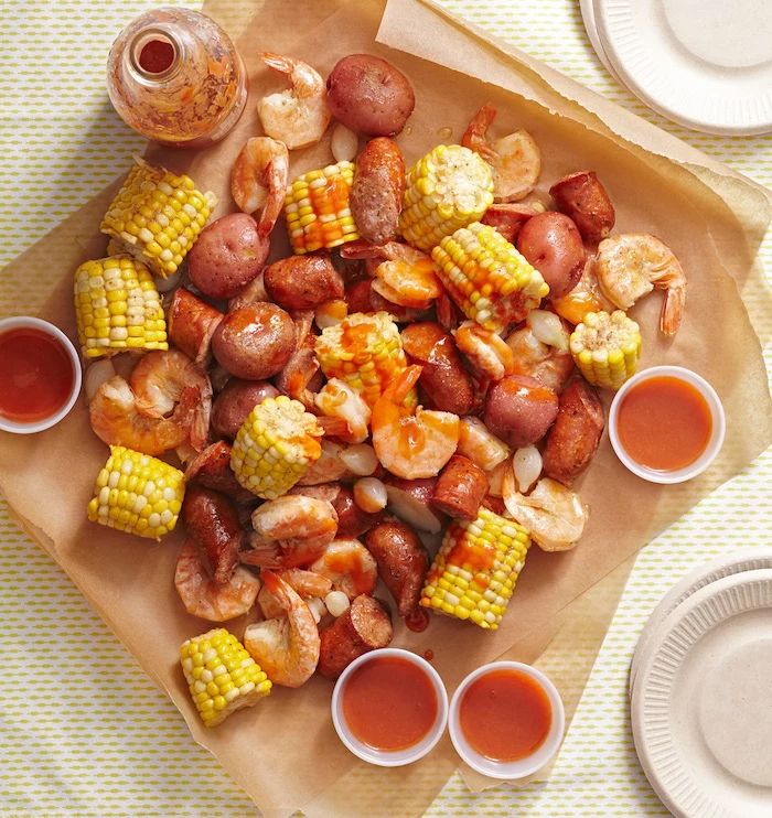 sauce in small bowls crab boil recipe corn on the cob sausages potatoes placed on paper lined table