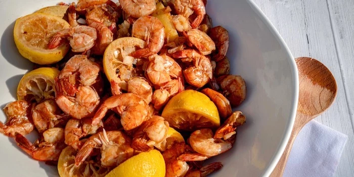 shrimp with lemon wedges seafood boil sauce placed in white bowl placed on white wooden table