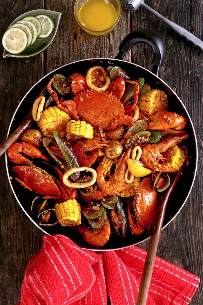 skillet with crabs corn on the cob oysters cajun seafood boil placed on wooden table