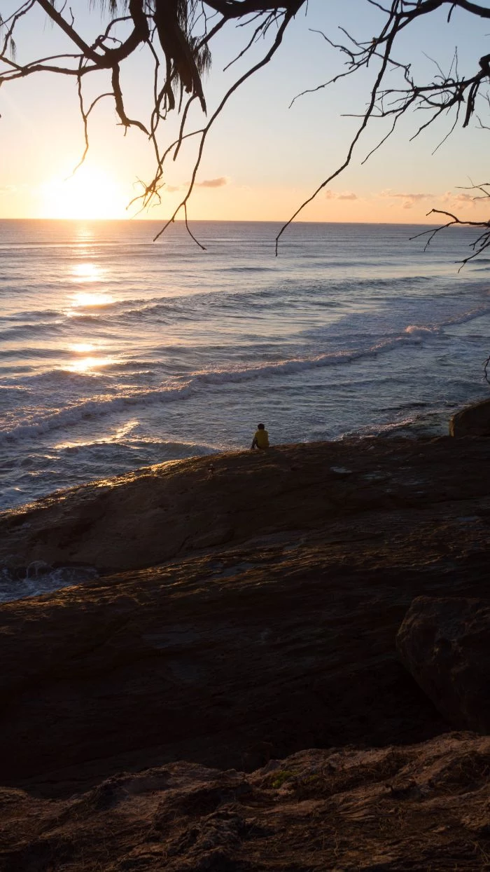 sun rising above the ocean beach background hd man sitting on rocks on the beach watching the sunrise