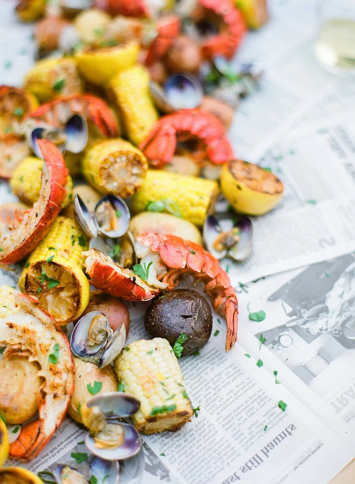 table covered with newspaper pages crab boil recipe corn on the cop potatoes lemon wedges garnished with parsley