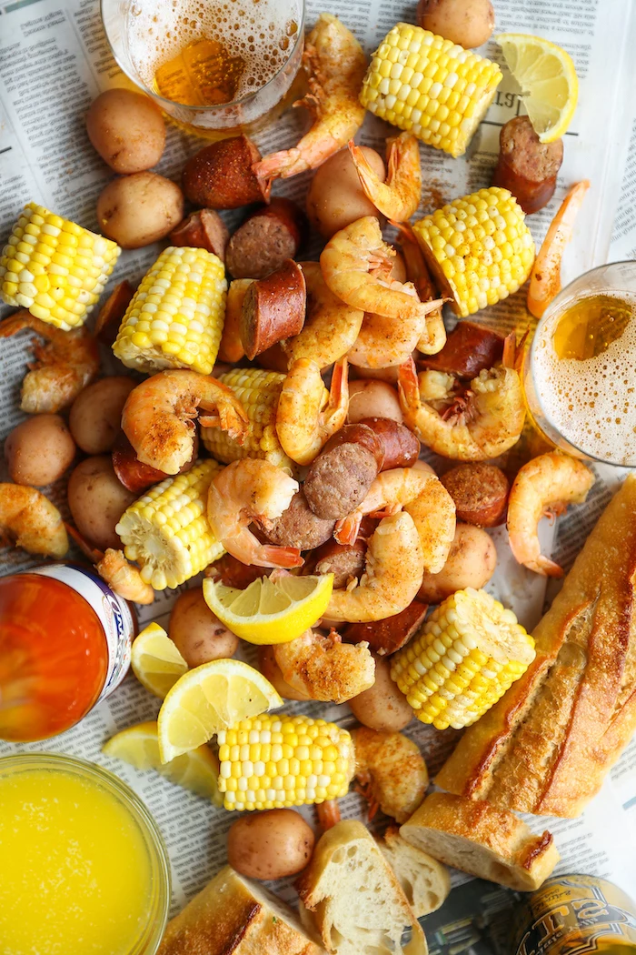 table covered with newspaper pages seafood boil sauce shrimp potatoes corn on the cob baguetta lemon wedges