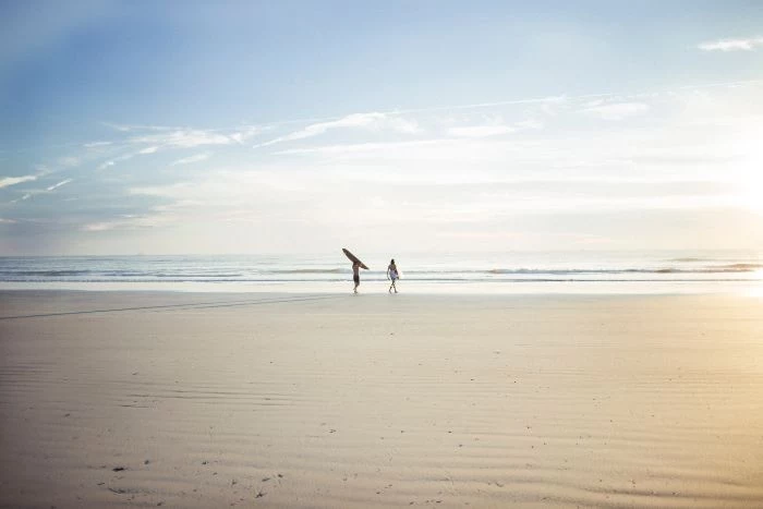 two people one holding surfboard walking on sandy beach beach wallpaper hd ocean in the distance