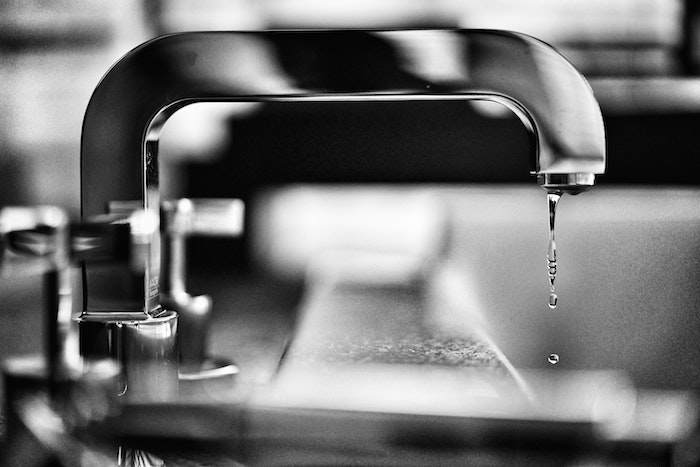 water dropping from metal tap professional plumbing services black and white photo