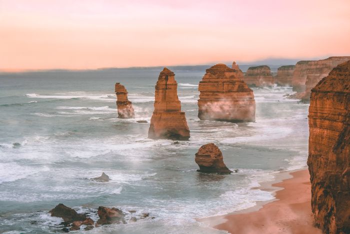 waves crashing into tall rock in the water beach wallpaper hd sunset photo