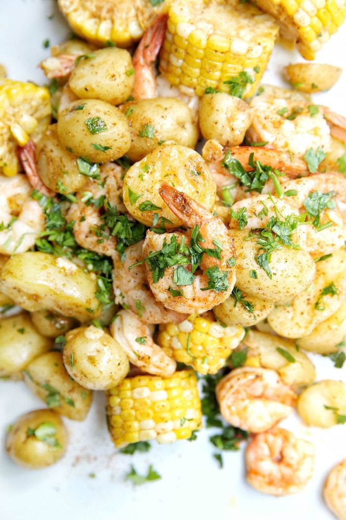 white plate filled with corn on the cob potatoes shrimp seafood boil recipe garnished with fresh parsley