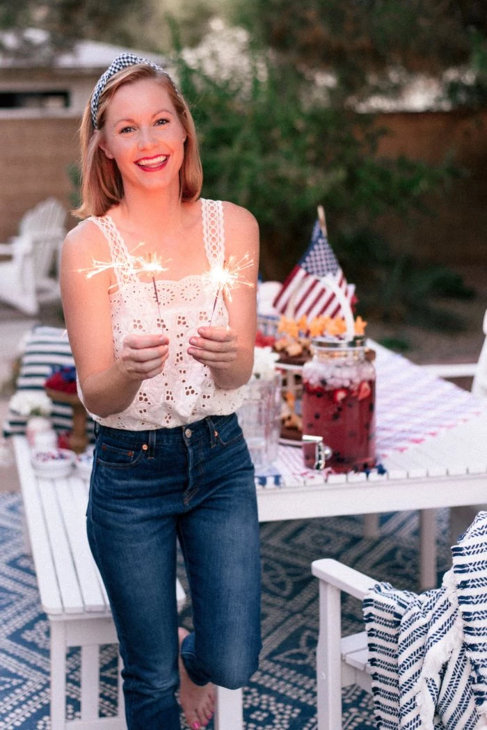 woman standing next to table decorated with american flags 4th of july outfits wearing jeans white lace top