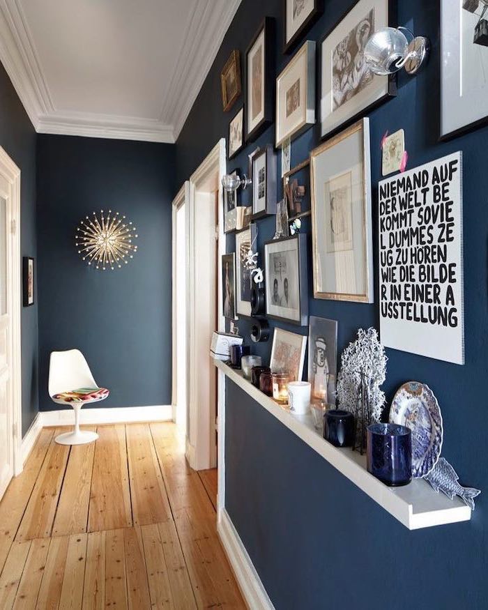 wooden floor dark blue walls narrow hallway ideas lots of framed art hanging on wall and on floating shelf