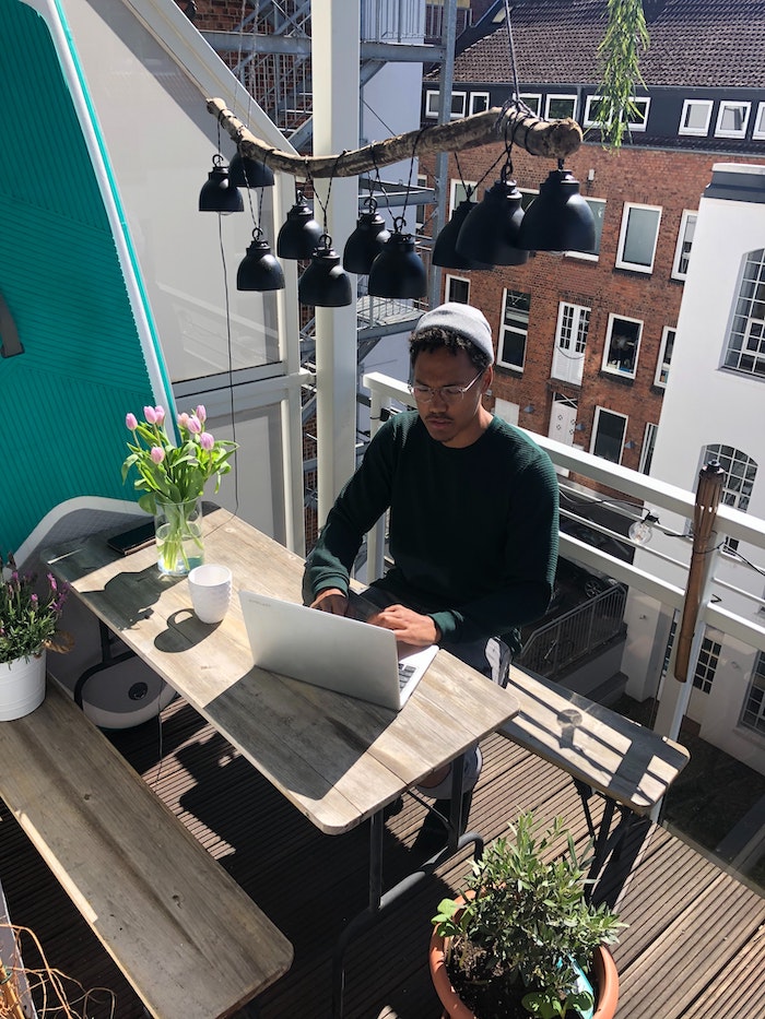 working from home man sitting on his balcony laptop opened on wooden table