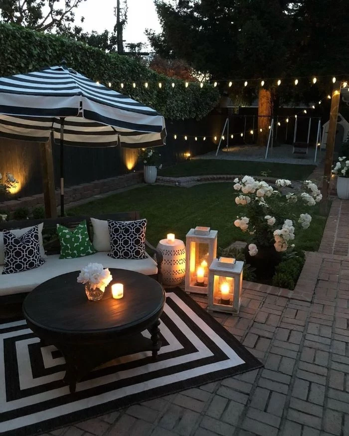 black wooden table with wooden bench next to it black and white rug and umbrella backyard ideas on a budget lanterns