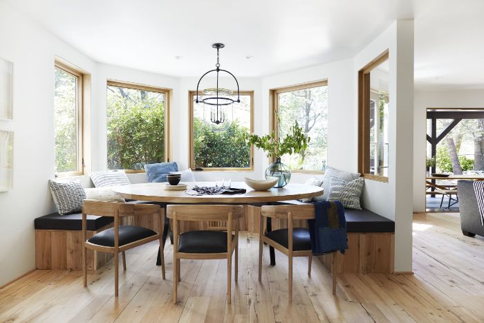 breakfast nook with round rustic dining table bench and chairs around it blue and white throw pillows