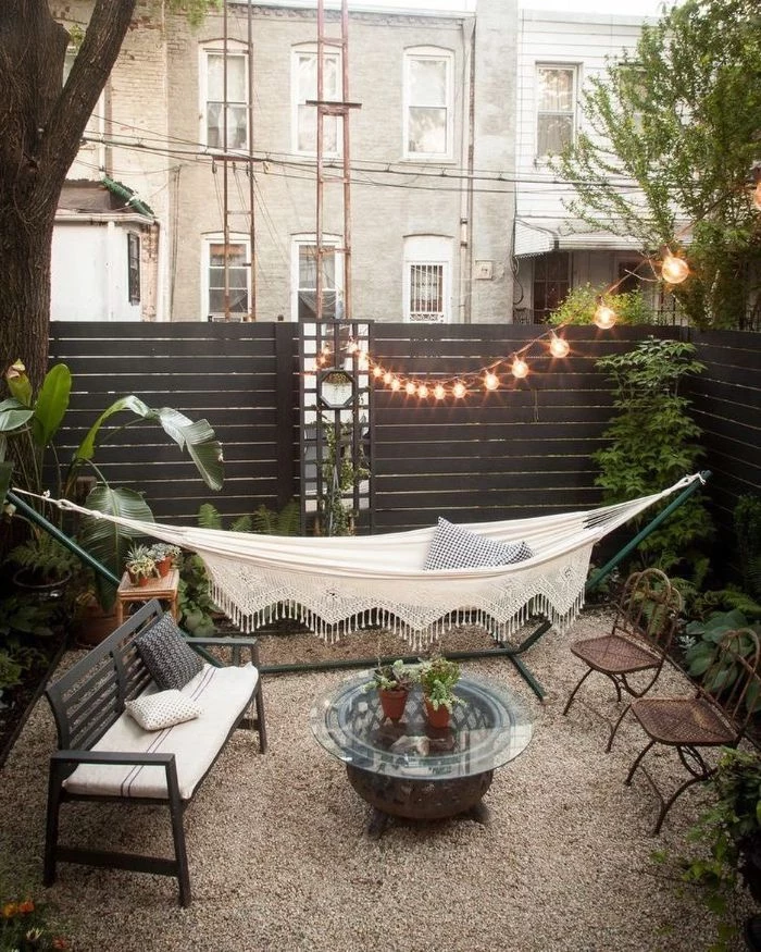 hammock wooden bench table and chairs placed on gravel diy backyard ideas fairy lights above them