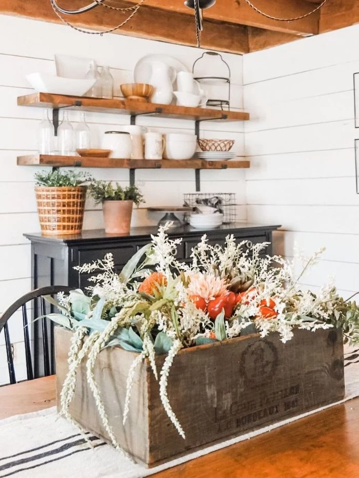 open shelving above black cupboard farmhouse table and chairs wooden crate with flowers on the table