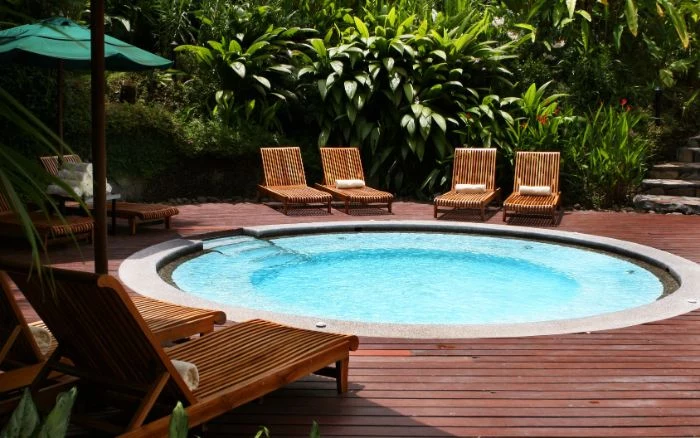 small round pool surrounded by wooden lounge chairs small backyard patio ideas lots of plants and trees