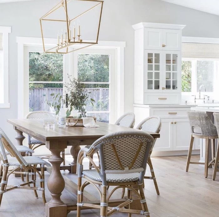 white walls and cupboards farmhouse kitchen table wooden chairs and large table chandelier hanging above it