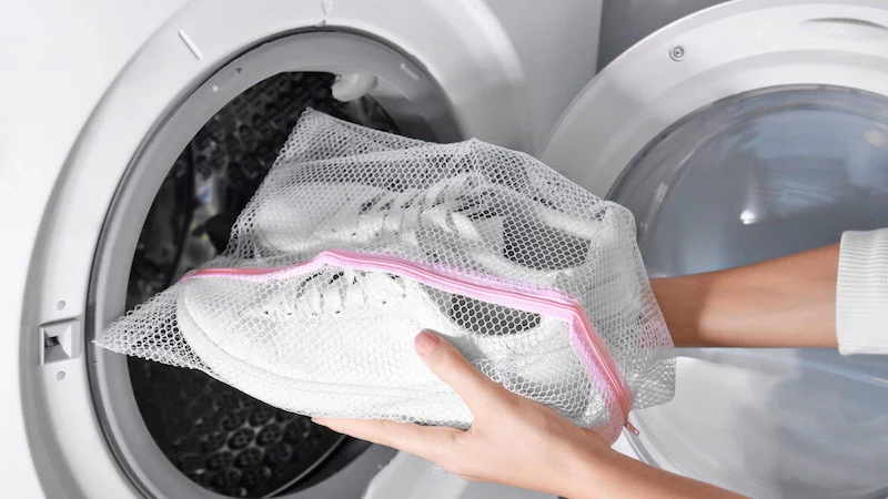 woman putting mesh with white sneakers into washing machine, closeup