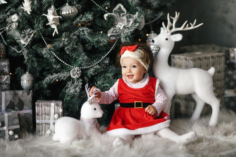 baby girl wearing santa dress sitting beside christmas tree 3329488