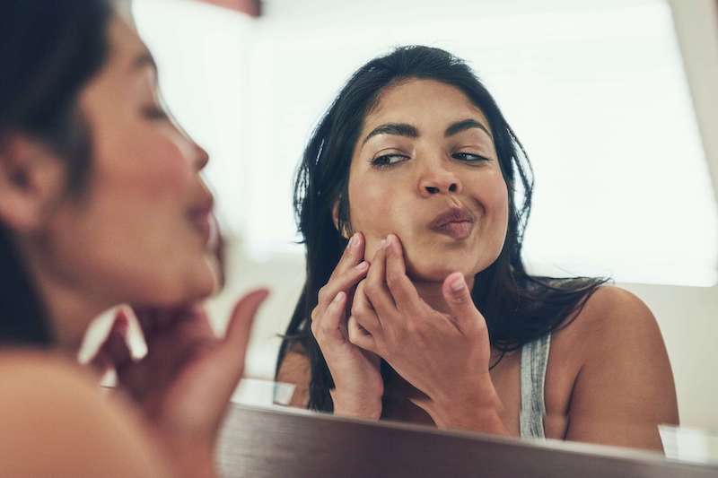 is adapalene a retinol woman picking at skin in mirror