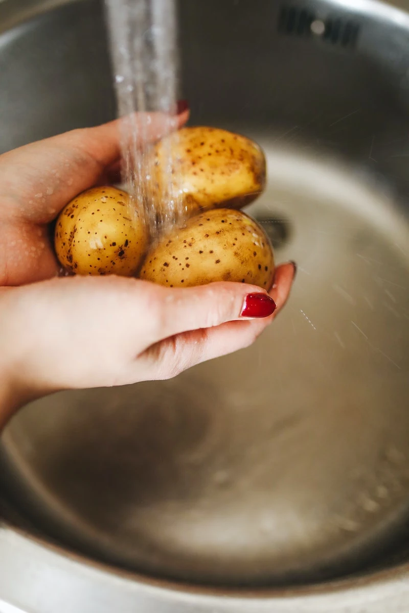 how to make potato wedges woman washing potatoes under the sink