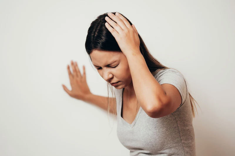 woman suffering from dizziness with difficulty standing up while leaning on wall