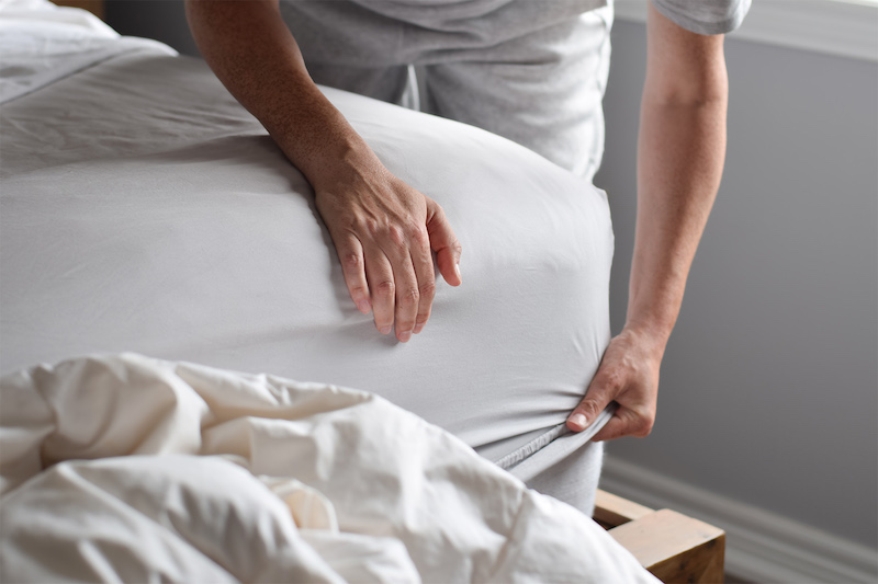 woman is putting on a fitted sheet on a mattress while making the bed