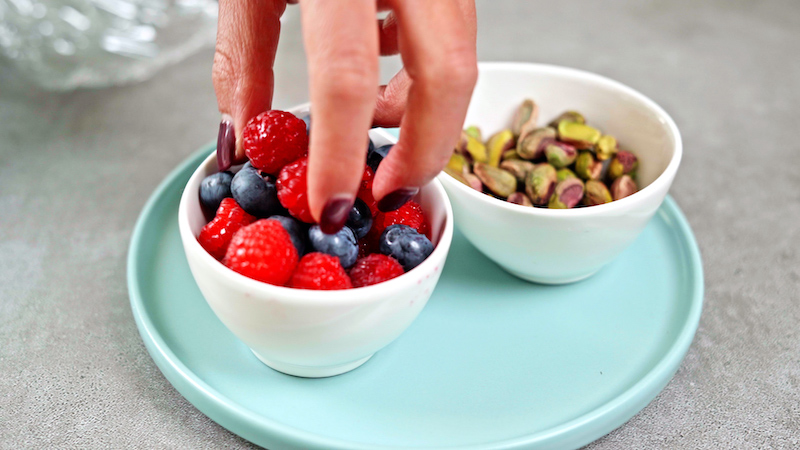 a hand grabbing berries from a bowl next to pistachios