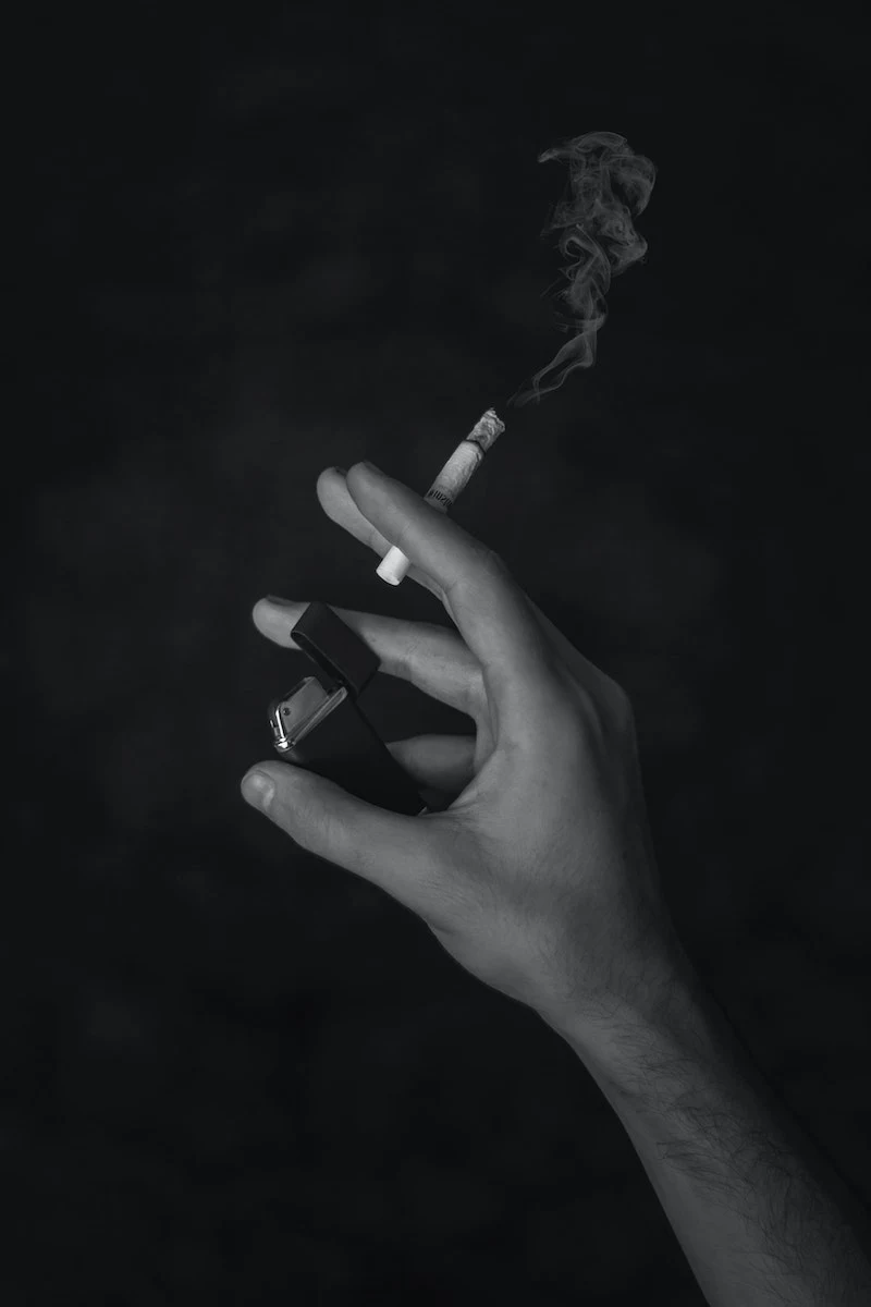 a hand holding a cigarette and lighter in black and white