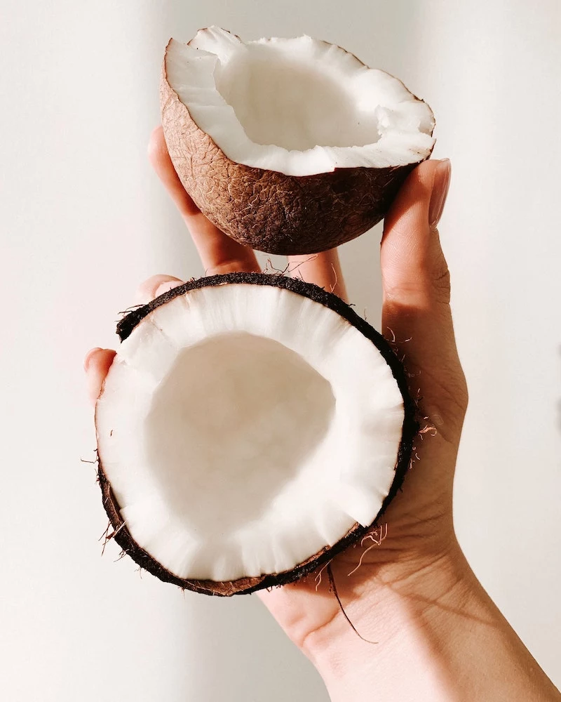 a hand holding a coconut split into two