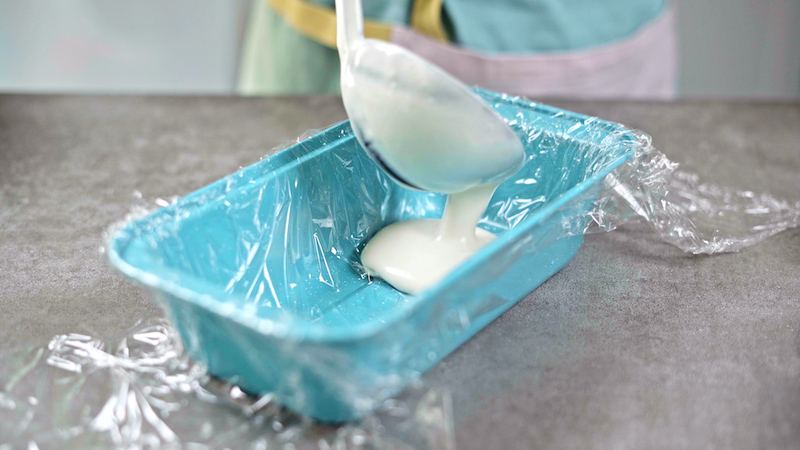 a ladle poring ice cream into a blue loaf pan
