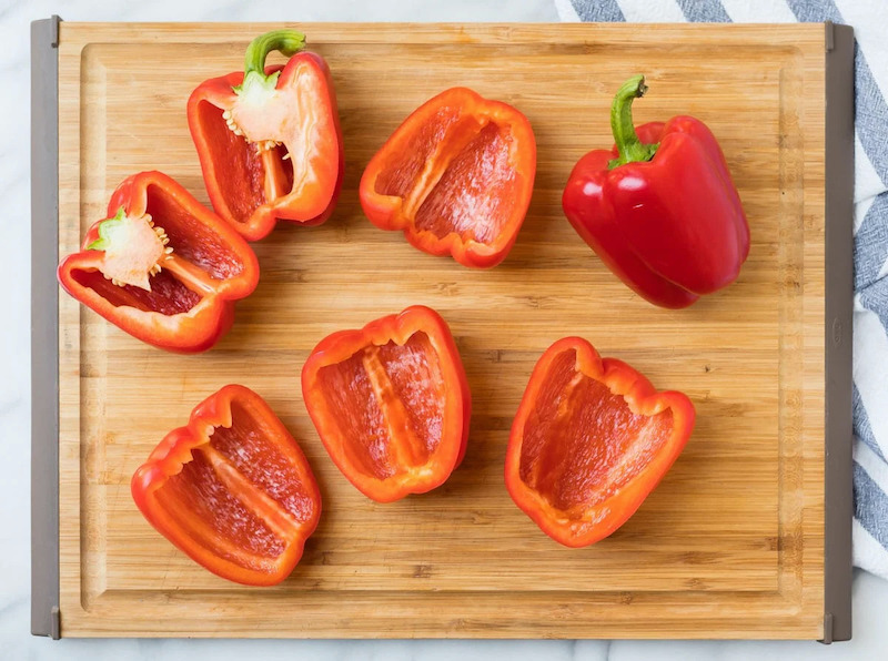 a whole pepper and halved red peppers on a wooden board