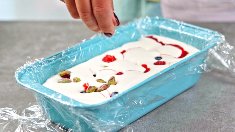 berries being spinkled over ice cream mixture in blue loaf pan