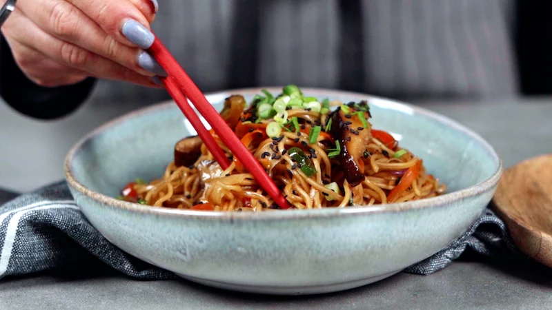 bowl of sweet and sour noodles with green onion and sesame seed garnish