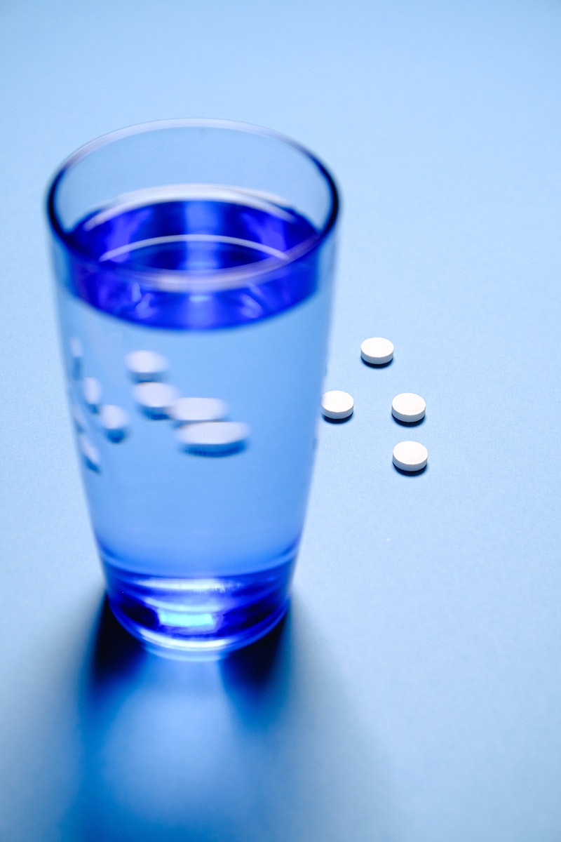 cup of water with painkillers on blue background
