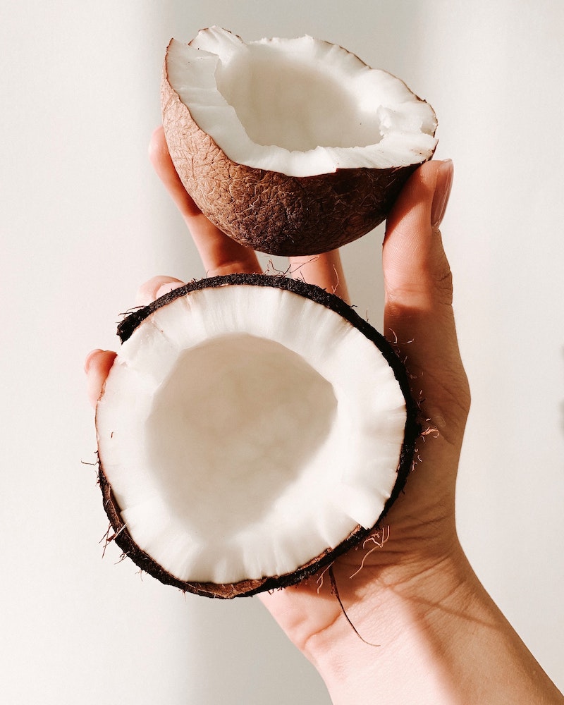 hand holding two coconut pieces sliced in half