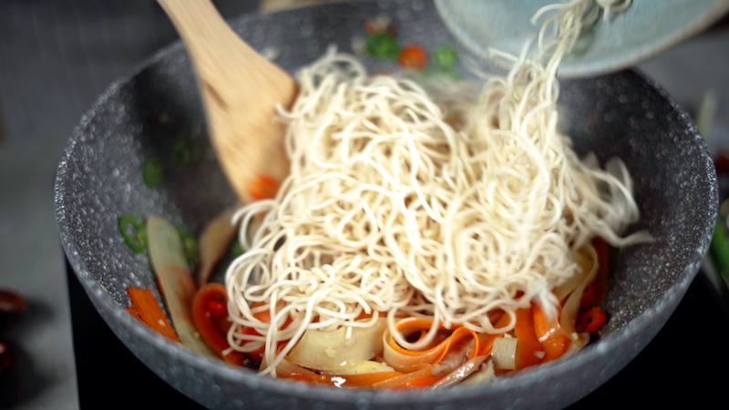 noodles being added to stir fry vegetables