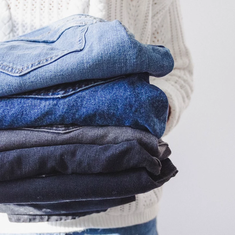 person holdin a pile of different jeans