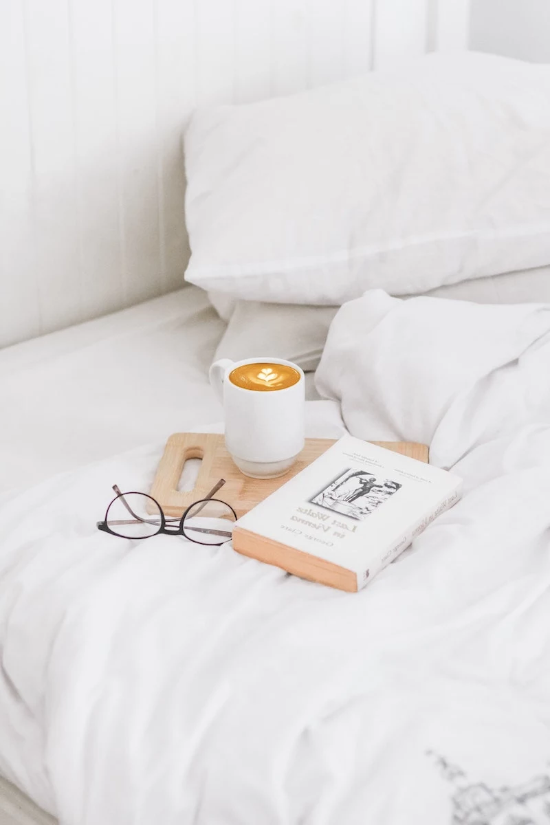 white sheets with a coffee and a book on the bed