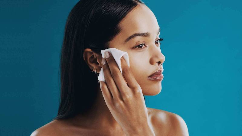 woman on blue background removing her makeup