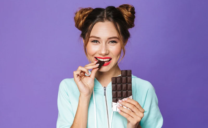 woman on purple background eating a chocolate bar