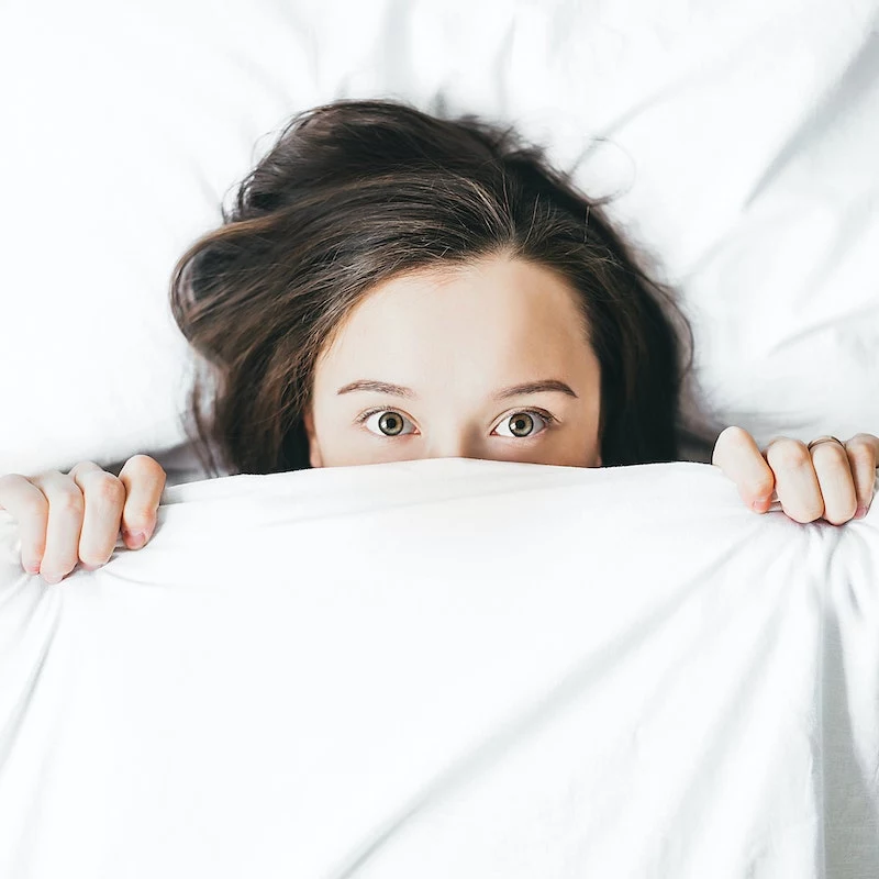 woman peaking from underneath the covers