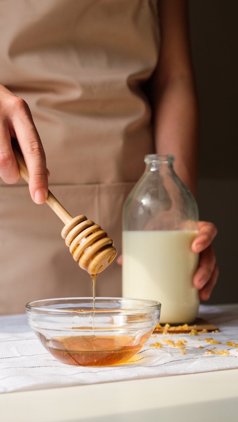 woman putting honey in bowl qith milk in background